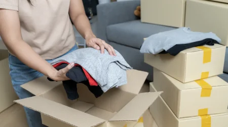 Frau sortiert gut erhaltene Kleidung in einem Raum mit Umzugskartons für die Wertanrechnung im Rahmen einer Entrümpelung.