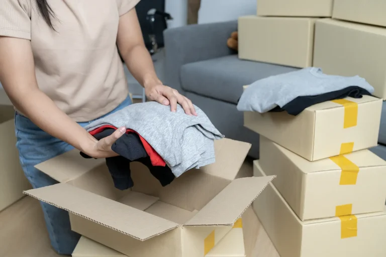 Frau sortiert gut erhaltene Kleidung in einem Raum mit Umzugskartons für die Wertanrechnung im Rahmen einer Entrümpelung.