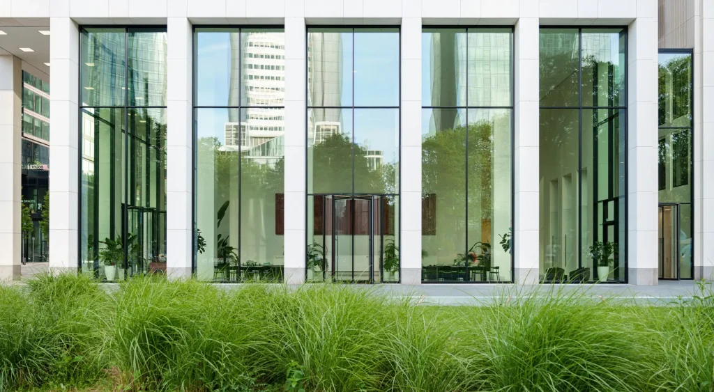 Großflächige Glasfassade eines modernen Bürogebäudes mit reflektierenden Fenstern, umgeben von gepflegtem Grün – regelmäßige Glasreinigung sorgt für klare Sicht und repräsentatives Erscheinungsbild.