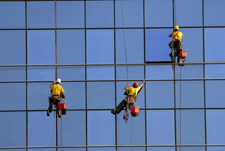 Drei Industriekletterer reinigen mit Sicherheitsausrüstung die Glasfassade eines Hochhauses – ein typischer Einsatzbereich in der professionellen Höhenreinigung urbaner Gebäude.