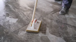 Ein Handwerker entfernt Zementschleiher auf frisch verlegten Bodenfliesen mit einem Schwammbrett.