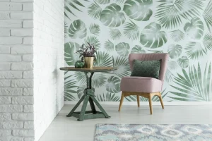 Tropische Mustertapete mit grünen Palm- und Monstera-Blättern als Blickfang in modernem Wohnzimmer mit rosa Sessel und weißer Ziegelwand.