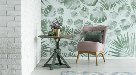 Tropische Mustertapete mit grünen Palm- und Monstera-Blättern als Blickfang in modernem Wohnzimmer mit rosa Sessel und weißer Ziegelwand.
