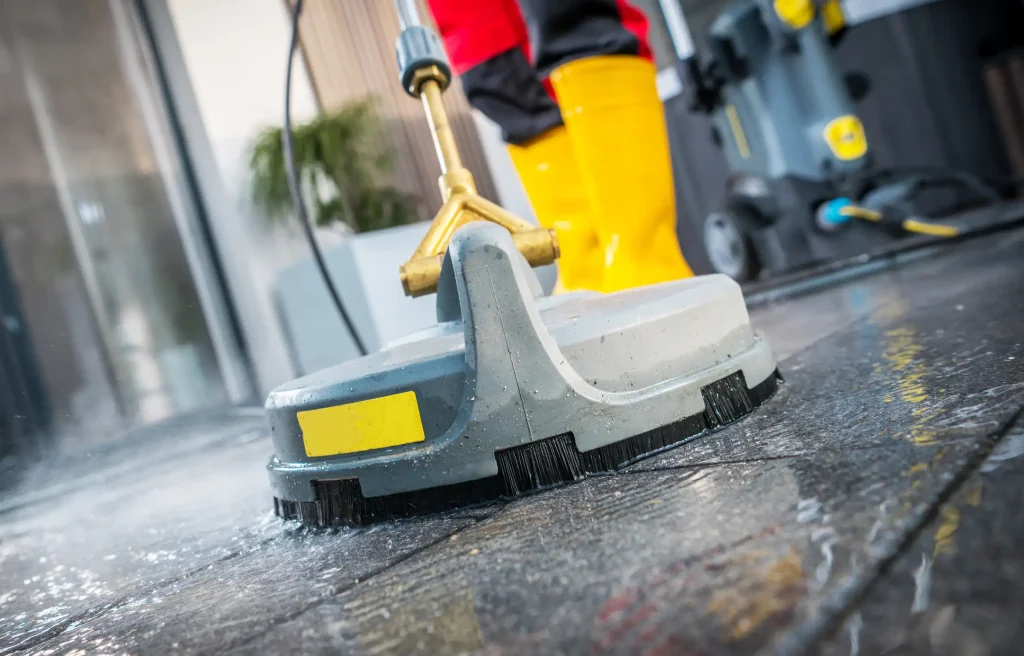 Arbeiter in gelben Gummistiefeln, bei der Reinigung von Fliesen mit einer professionellen Hochdruckbürste direkt nach der Verlegung.