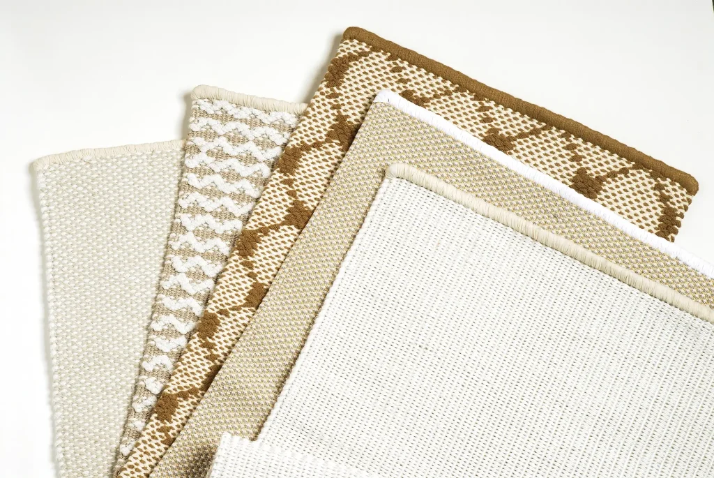 Musterstücke aus Sisalteppichen in verschiedenen Beige- und Brauntönen, nebeneinander auf weißem Hintergrund arrangiert.