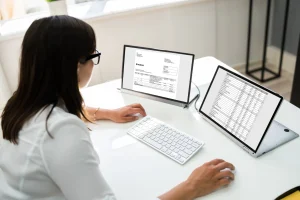 Eine Frau sitzt an ihrem Schreibtisch vor Laptop und versendet E-Rechnungen.