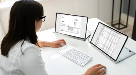 Eine Frau sitzt an ihrem Schreibtisch vor Laptop und versendet E-Rechnungen.
