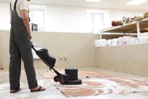 Mann in Arbeitshose shampooniert mit einer Einscheibenreinigungsmaschine einen Teppich im Rahmen einer professionellen Teppichreinigung.