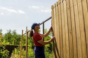Handwerker richtet mit Wasserwaage einen neuen Sichtschutzzaun aus Holz im Garten aus – symbolisch für professionelle Zaunmontage, Gartenbau oder Renovierungsarbeiten im Außenbereich.