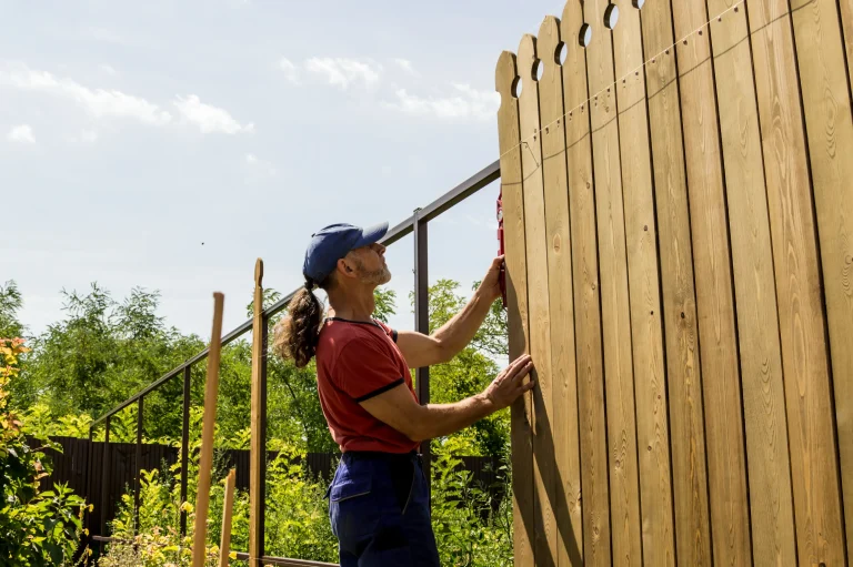 Handwerker richtet mit Wasserwaage einen neuen Sichtschutzzaun aus Holz im Garten aus – symbolisch für professionelle Zaunmontage, Gartenbau oder Renovierungsarbeiten im Außenbereich.