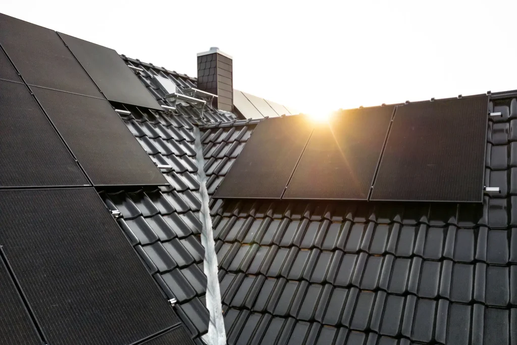 Kreuzsatteldach mit dunklen Dachziegeln, bei dem zwei Satteldächer rechtwinklig aufeinandertreffen. Entlang der Dachkehle, wo sich die beiden Dachflächen schneiden, ist eine Metallrinne zur Ableitung von Regenwasser angebracht. Auf beiden Dachflächen sind schwarze Solarpaneele montiert.