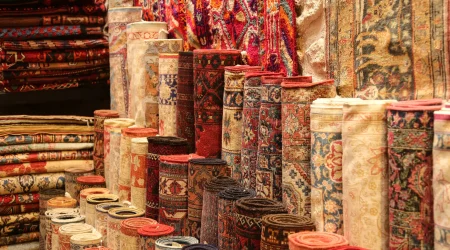 Vielzahl aufgerollter und gefalteter orientalischer Teppiche mit detailreichen Mustern in warmen Rottönen, ausgestellt in einem traditionellen Teppichgeschäft.