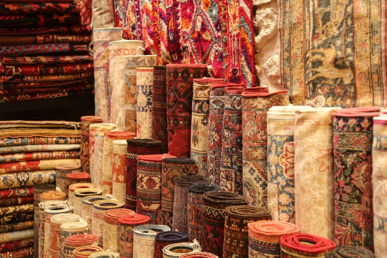 Vielzahl aufgerollter und gefalteter orientalischer Teppiche mit detailreichen Mustern in warmen Rottönen, ausgestellt in einem traditionellen Teppichgeschäft.