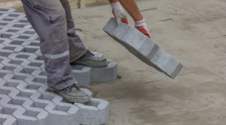 Ein Gartenbauer beim Verlegen von schweren Rasengittersteinen aus Beton auf vorbereiteten Untergrund.