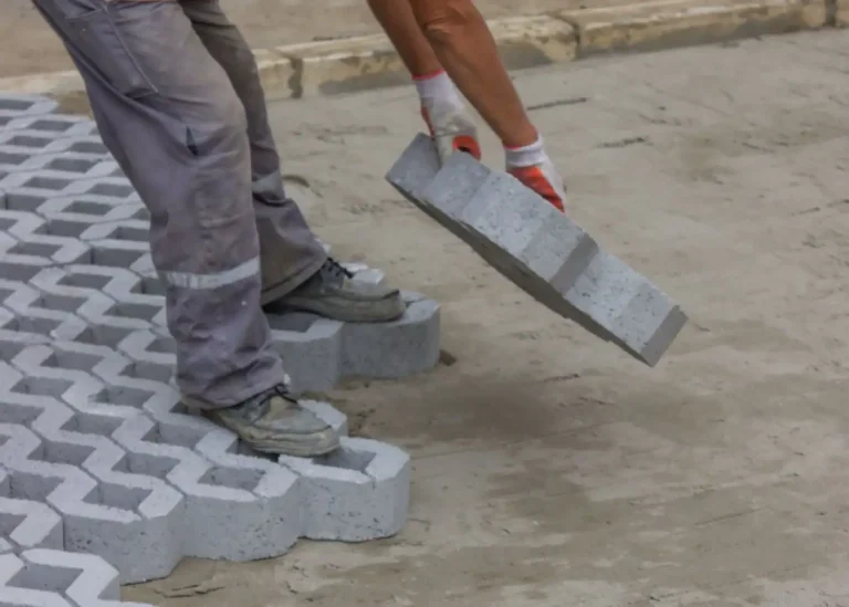 Ein Gartenbauer beim Verlegen von schweren Rasengittersteinen aus Beton auf vorbereiteten Untergrund.