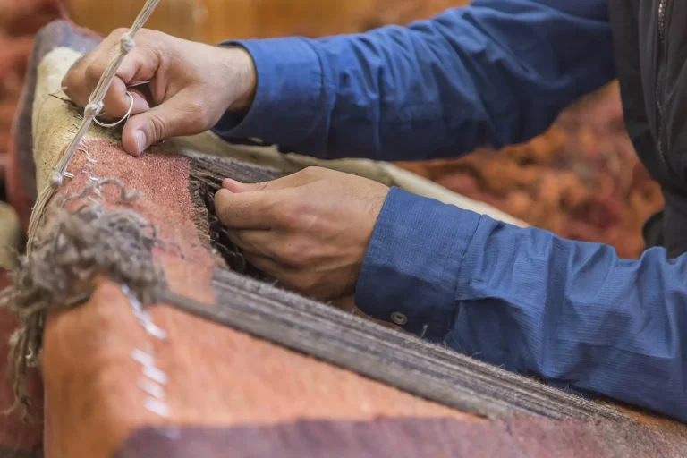 Reparatur in Handarbeit an einem traditionellen Teppich mit Nadel und Faden in einem Webrahmen.