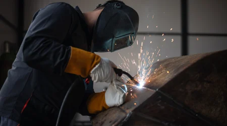Ein Handwerker mit einem Schweißgerät und einer Schweißermaske bei der Arbeit.