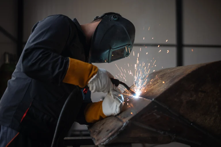 Ein Handwerker mit einem Schweißgerät und einer Schweißermaske bei der Arbeit.