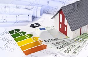 Energieeffizienzklasse eines Hauses: Modellhaus auf Bauplänen mit Euroscheinen und Energieausweis von A bis G.