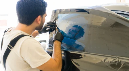 Ein Fahrzeugfolierer bringt eine Tönungsfolie präzise an der Seitenscheibe eines Autos an, um UV- und Hitzeschutz im Innenraum zu gewährleisten.