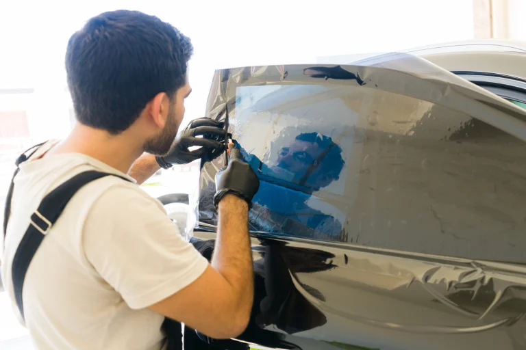 Ein Fahrzeugfolierer bringt eine Tönungsfolie präzise an der Seitenscheibe eines Autos an, um UV- und Hitzeschutz im Innenraum zu gewährleisten.