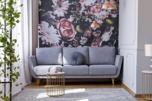 Fototapete an einer Wand eines Wohnzimmers. Vor der Wand steht ein graues Sofa. Darüber hängen zwei Pendelleuchten in Kupferoptik.