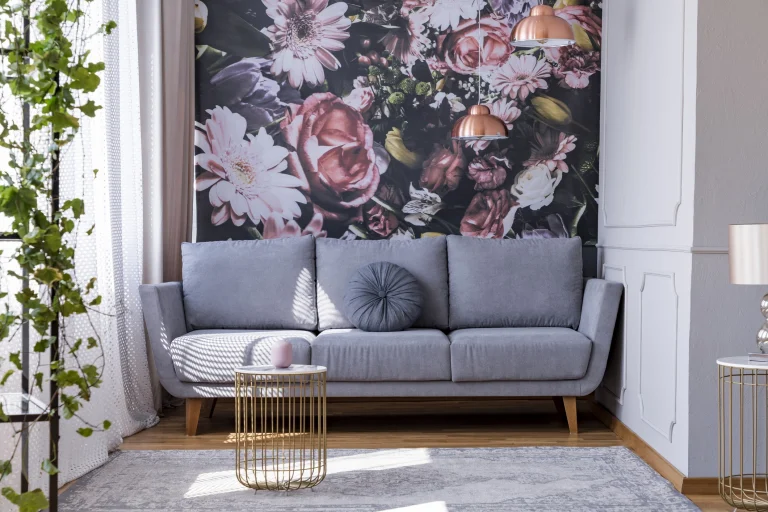 Fototapete an einer Wand eines Wohnzimmers. Vor der Wand steht ein graues Sofa. Darüber hängen zwei Pendelleuchten in Kupferoptik.