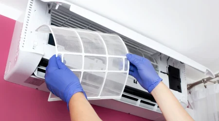 Ein Klimatechniker mit blauen Schutzhandschuhen entnimmt den Filter einer an der Wand montierten Klimaanlage zur Reinigung.