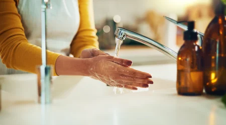 Frau in gelben Sweatshirt wäscht sich ihre Hände unter einem Wasserhahn.