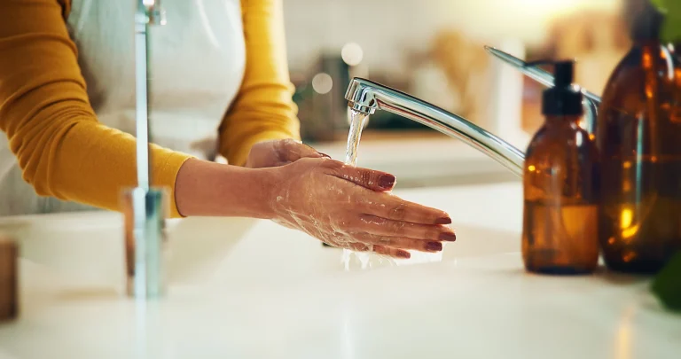Frau in gelben Sweatshirt wäscht sich ihre Hände unter einem Wasserhahn.
