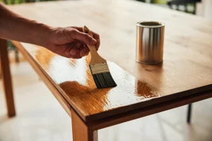 Ein Mann lasiert seinen Holztisch um ihn vor Umwelteinflüssen zu schützen.