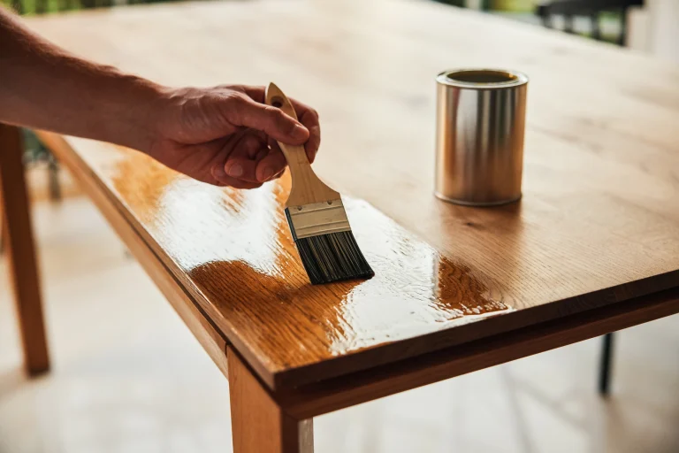 Ein Mann lasiert seinen Holztisch um ihn vor Umwelteinflüssen zu schützen.
