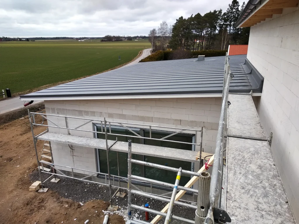 Modernes Pultdach mit dunkler Metallabdeckung auf einem Neubau, aufgenommen von einem Gerüst an der unverputzten Fassade.