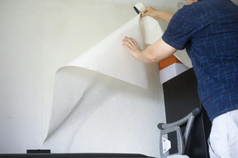 Ein Tapezierer bringt eine weiße Tapetenbahn an einer Wand an und glättet sie mit der Hand während der Tapezierarbeit.