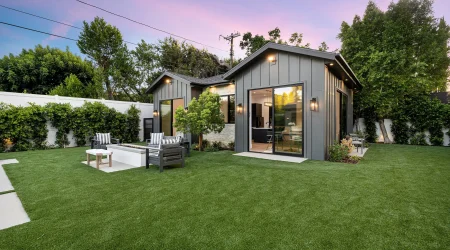 Modernes Tiny House im Bungalowstil mit Flachdach-Elementen und Holzverschalung, großer Fensterfront und gepflegtem Garten mit Lounge-Sitzbereich.