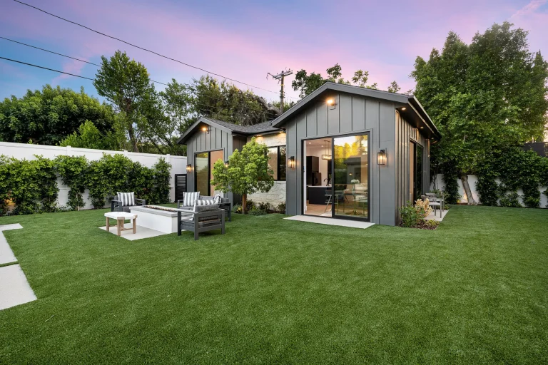 Modernes Tiny House im Bungalowstil mit Flachdach-Elementen und Holzverschalung, großer Fensterfront und gepflegtem Garten mit Lounge-Sitzbereich.