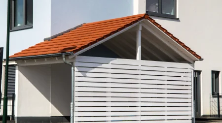 Carport mit Satteldach und Ziegeldeckung, Seitenverkleidung aus horizontalen weißen Holzlatten.