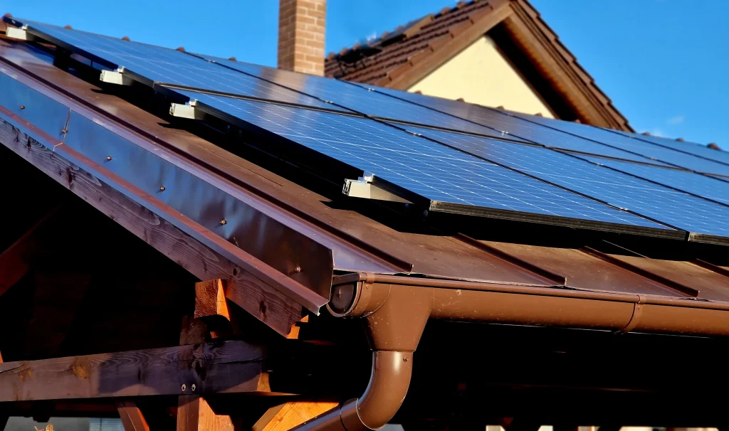 Solaranlage auf einem Schrägdach eines Carports mit braunem Metalldach und hölzerner Dachkonstruktion, Photovoltaikmodule zur Stromerzeugung sind in Reihen montiert.