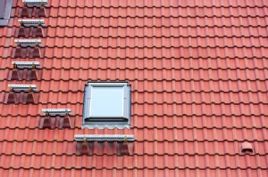 Dachfläche mit roten Ziegeln, einem Dachausstiegsfenster und mehreren Dachstufen als Steighilfen.