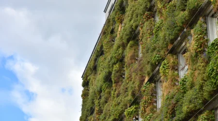Begrünte Fassade mit vertikal angeordneten Pflanzmodulen an mehrstöckigem Gebäude vor bewölktem Himmel.