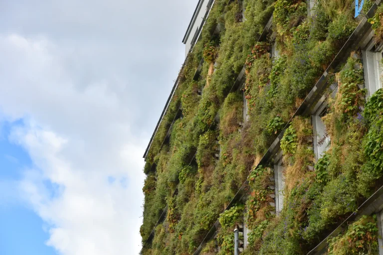 Begrünte Fassade mit vertikal angeordneten Pflanzmodulen an mehrstöckigem Gebäude vor bewölktem Himmel.
