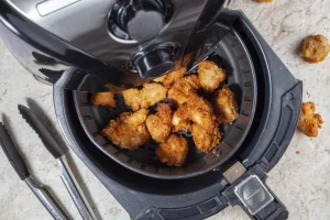 Heißluftfritteuse von oben mit geöffnetem Fach, in dem knusprige Hänchenteile liegen.