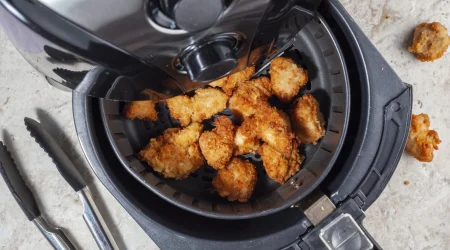 Heißluftfritteuse von oben mit geöffnetem Fach, in dem knusprige Hänchenteile liegen.