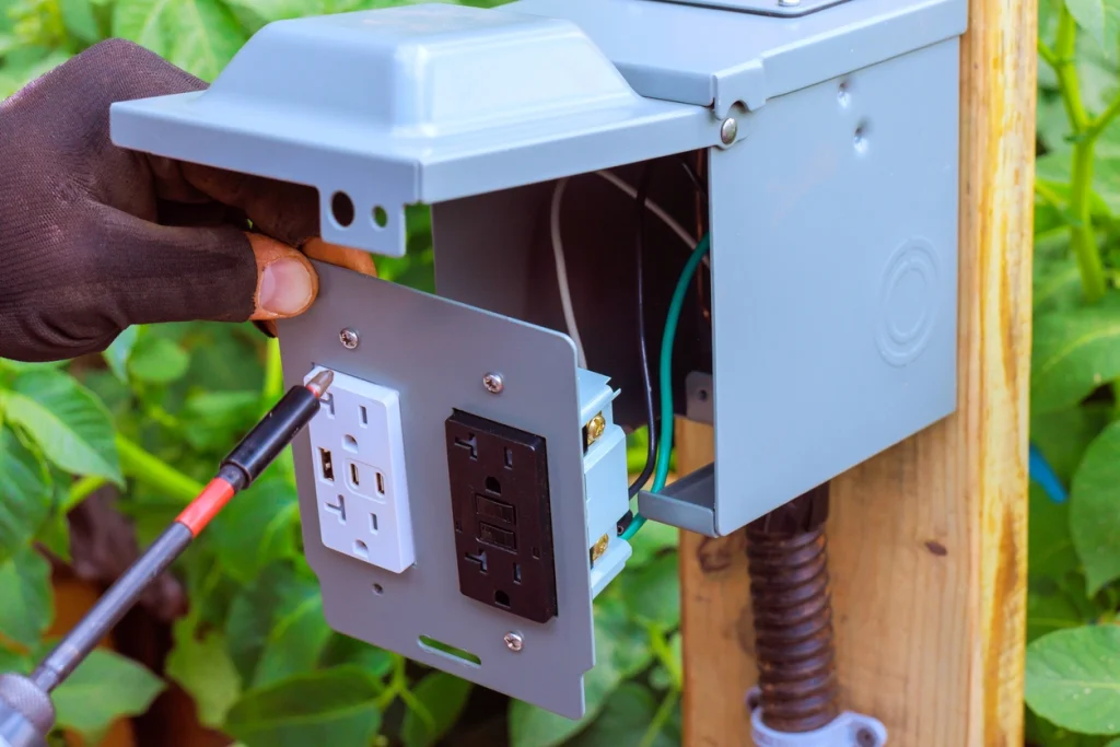 Elektriker installiert wetterfeste Außensteckdose an Holzpfosten im Außenbereich