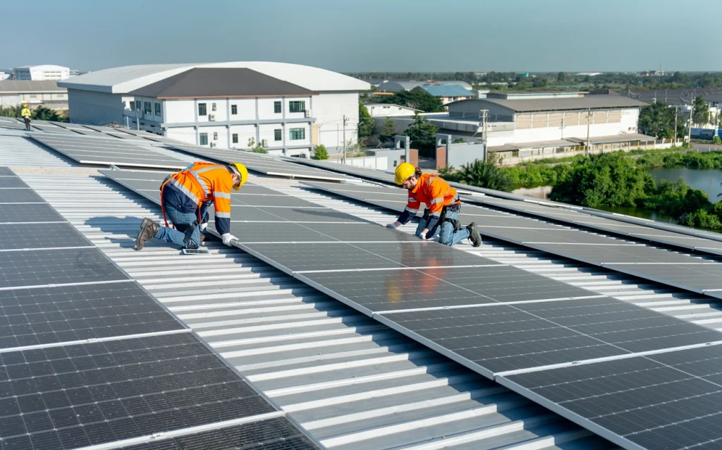 Zwei Techniker installieren Solarmodule auf einem Dach zur Nutzung von Solarenergie