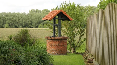 Wasserbohrloch mit Wasserauslass in grünem, gepflegtem Garten mit Gras und Pflanzen