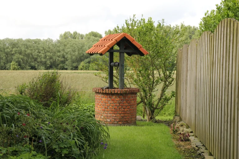 Wasserbohrloch mit Wasserauslass in grünem, gepflegtem Garten mit Gras und Pflanzen
