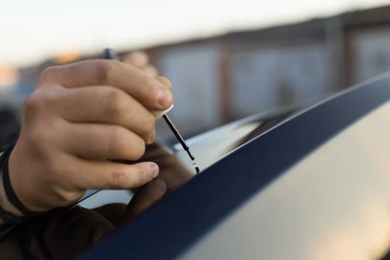 Eine Hand mit einem Lackausbesserungsstift auf einer Motorhaube
