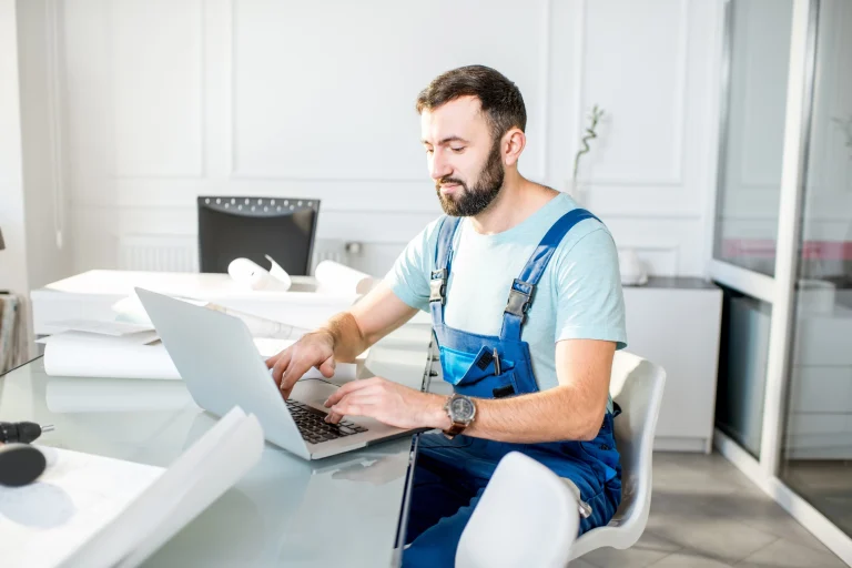 Ein Handwerker in Blaumann am Laptop bei der Büroarbeit