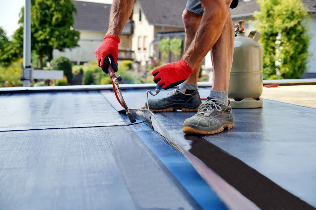 Handwerker dichtet ein Carportdach mit Dachpappe und Gasbrenner sorgfältig ab.
